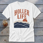 A white t-shirt featuring the text HOLLER LIFE above a sunset landscape graphic with mountains.