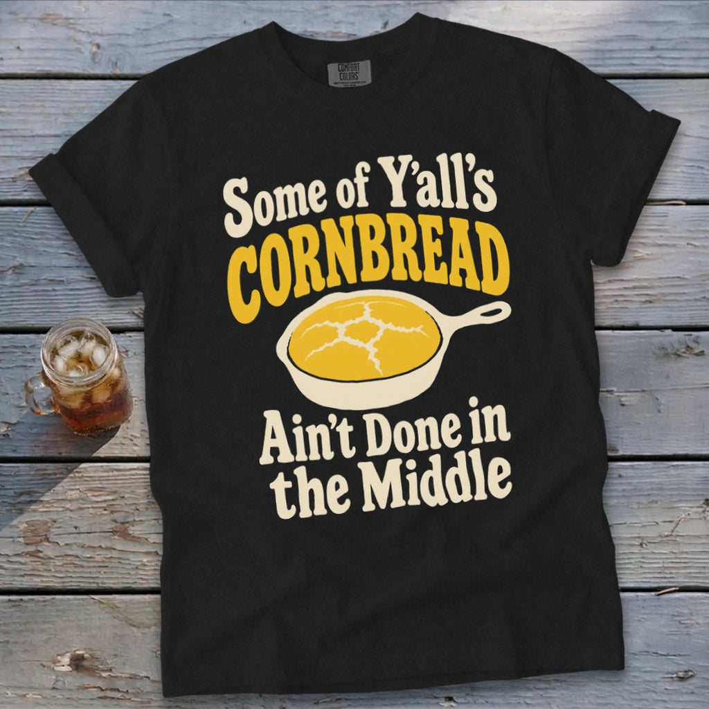 A black t-shirt with the text "Some of Y'all's CORNBREAD Ain't Done in the Middle" surrounding a skillet illustration.