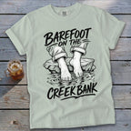 Light green t-shirt with "Barefoot on the Creek Bank" graphic and feet in water.