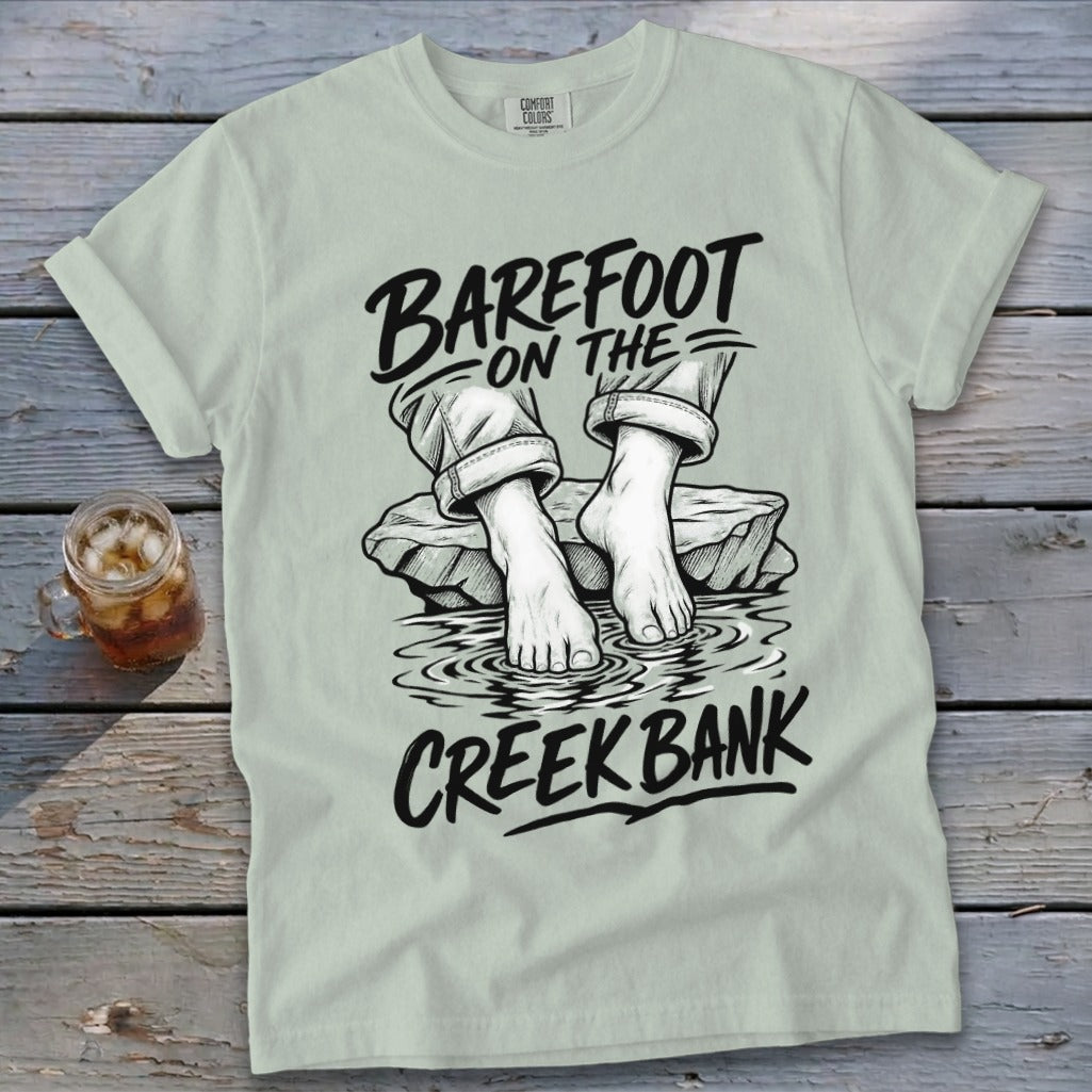 Light green t-shirt with "Barefoot on the Creek Bank" graphic and feet in water.
