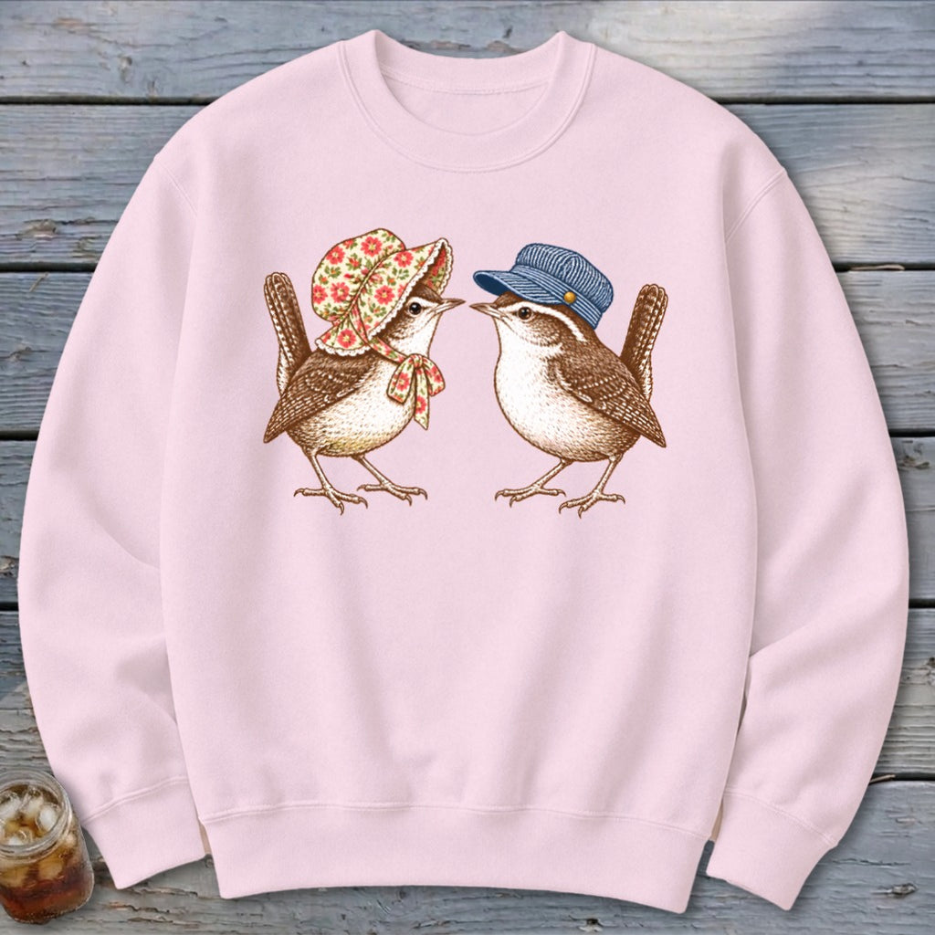 Pink sweatshirt featuring two wrens, one wearing a floral bonnet and bow, the other a blue cap.