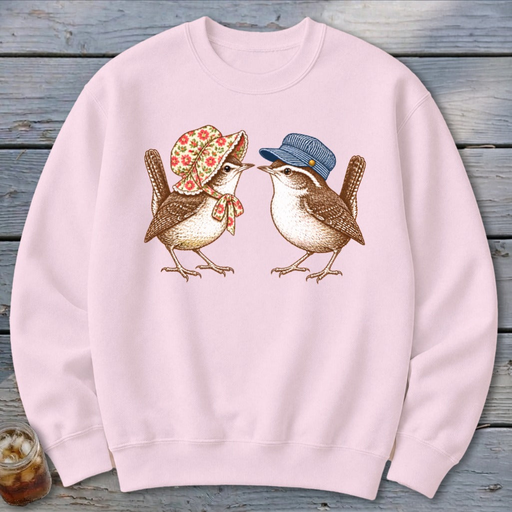 Pink sweatshirt featuring two wrens, one wearing a floral bonnet and bow, the other a blue cap.