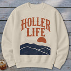 Beige crewneck sweatshirt featuring the text HOLLER LIFE above a sunset mountain landscape.