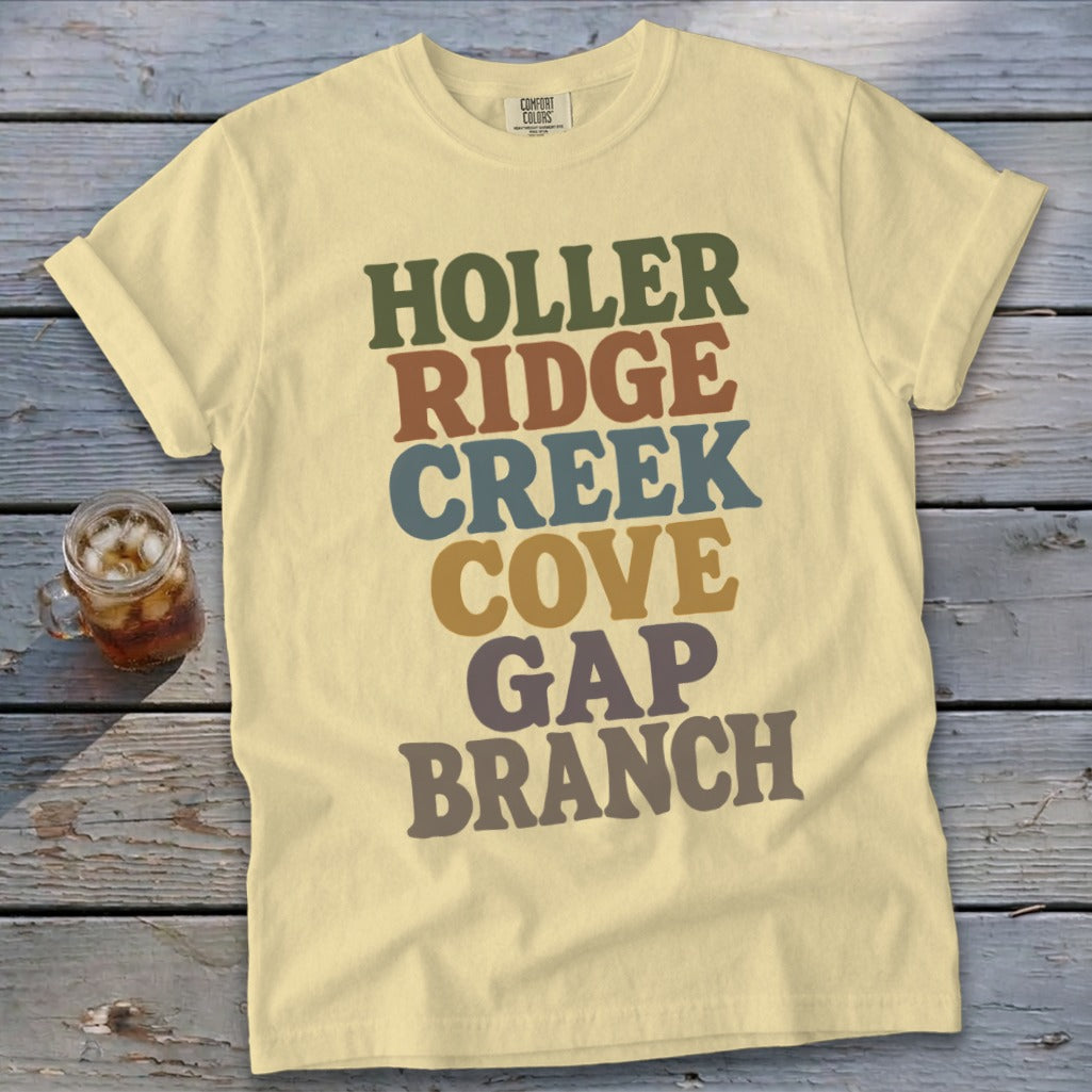 A light yellow t-shirt with multi-colored stacked text reading HOLLER RIDGE CREEK COVE GAP BRANCH.