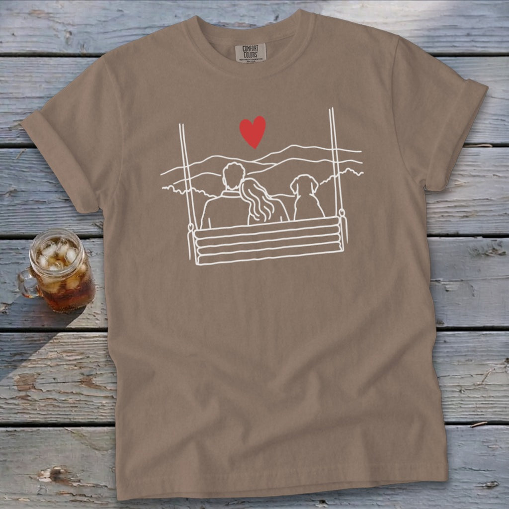 Brown t-shirt with white outline drawing of couple and dog on a swing, red heart.