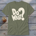 An olive green t-shirt with the cream text "Do What?" printed on the front, displayed on a wooden surface next to a glass of iced tea.