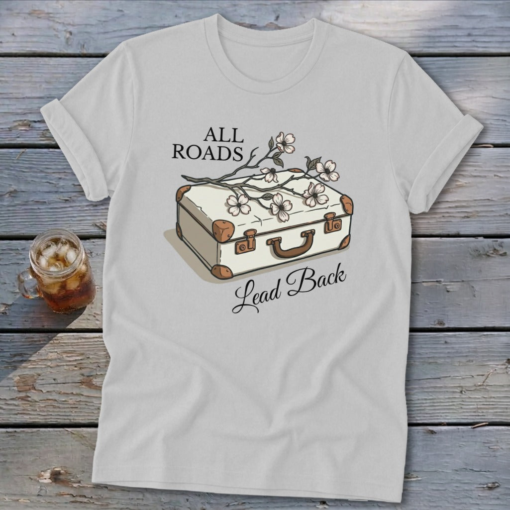 White t-shirt with a vintage suitcase and floral illustration and text "ALL ROADS Lead Back".