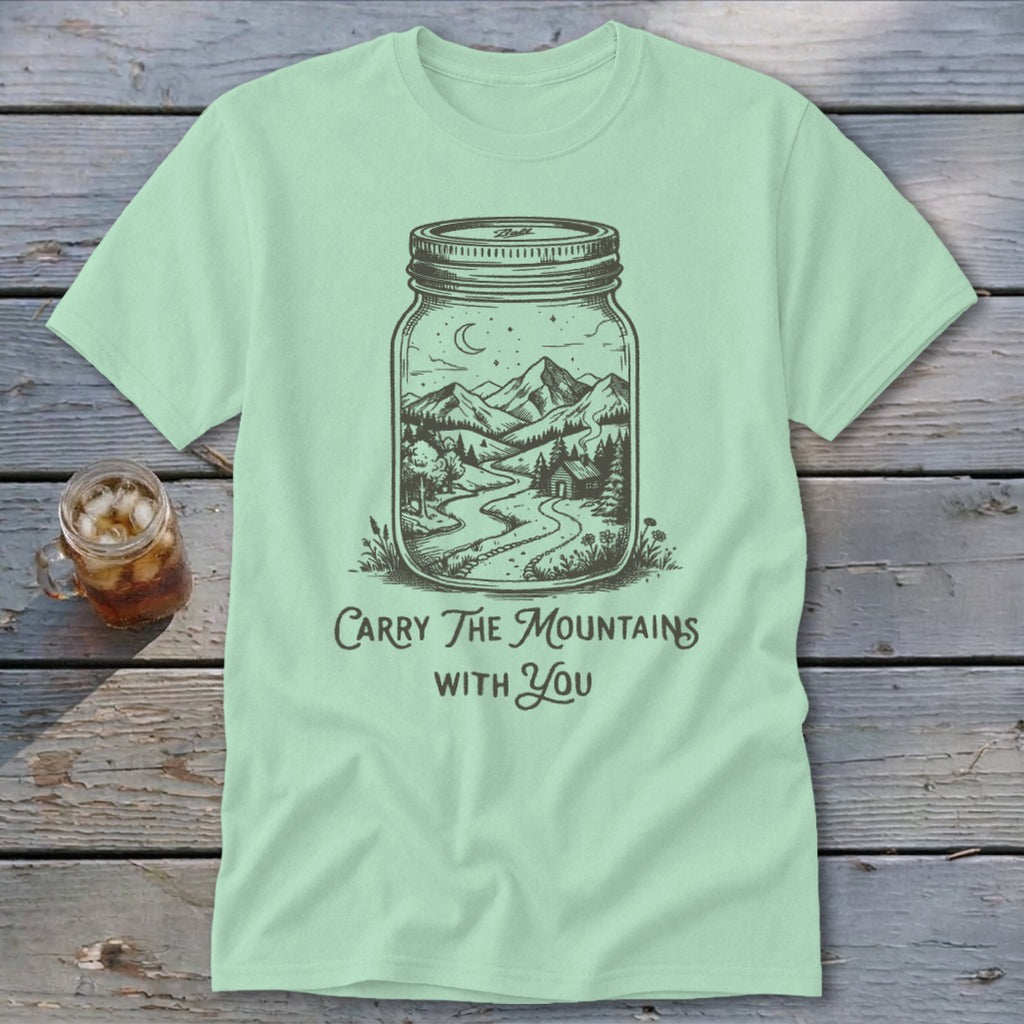 A light green t-shirt featuring a mason jar with a mountain landscape and the text Carry The Mountains With You.