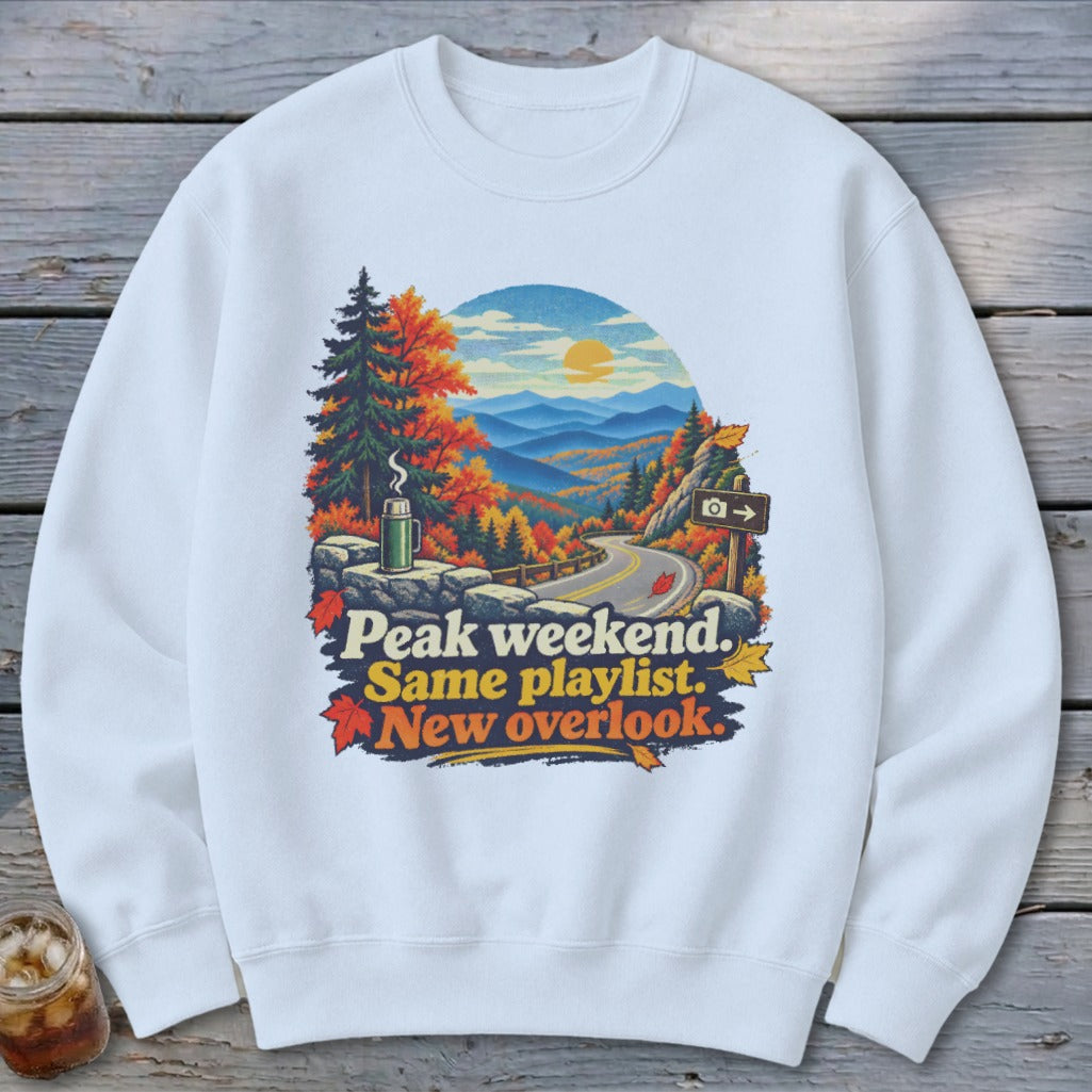 White sweatshirt with autumn mountain overlook graphic and text "Peak weekend. Same playlist. New overlook."