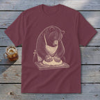 Bear wearing apron kneading dough on a cutting board, illustrated graphic on a maroon t-shirt.