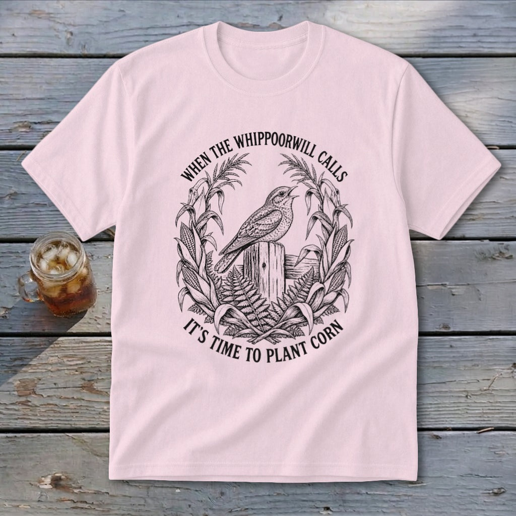 A light pink crewneck t-shirt featuring a vintage botanical illustration of a whippoorwill and cornstalks, with the text When The Whippoorwill Calls It's Time To Plant Corn.