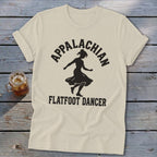 A cream-colored t-shirt featuring a black silhouette of a dancer with text reading "APPALACHIAN FLATFOOT DANCER."