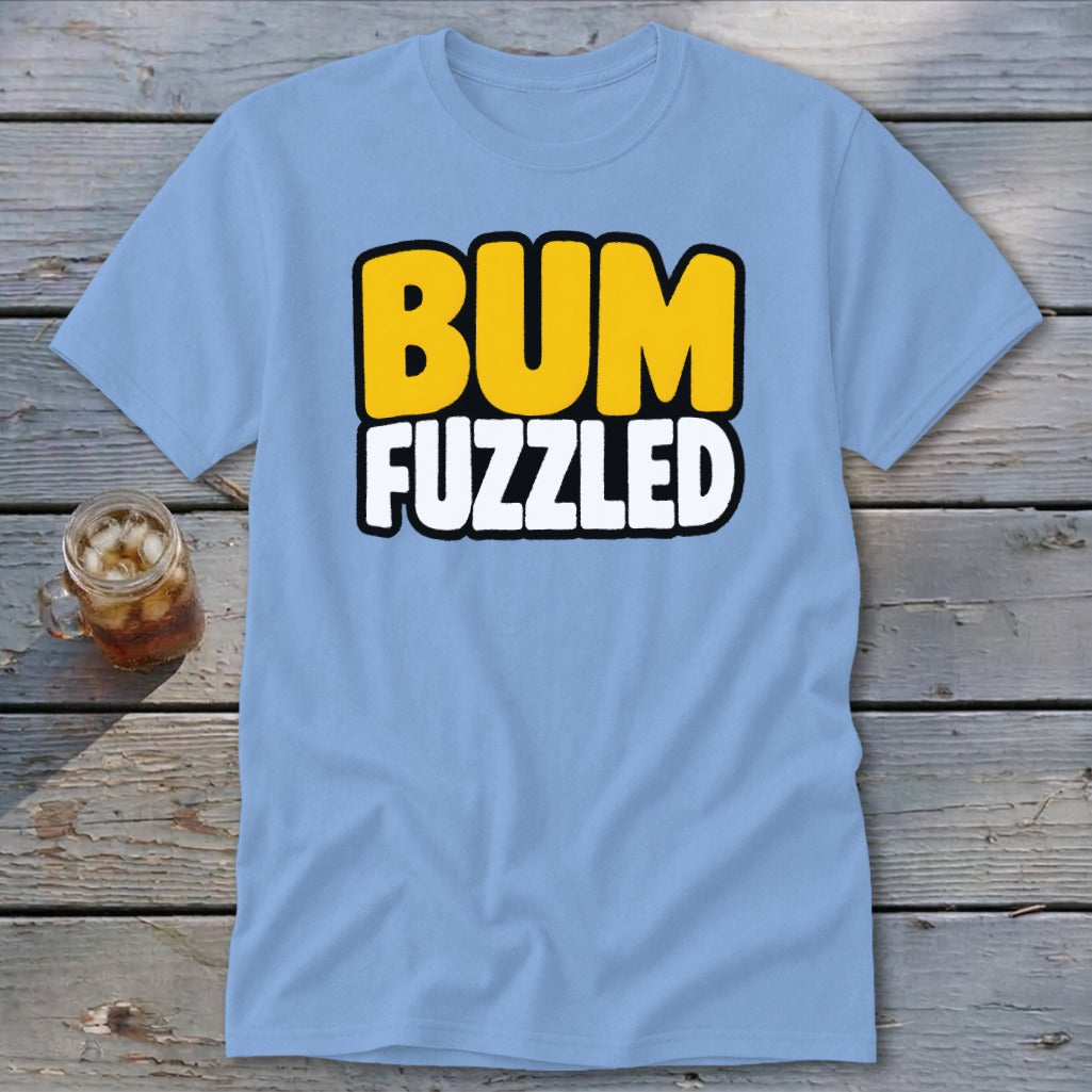 Light blue t-shirt featuring the text "BUM FUZZLED" in yellow and white, lying on a wooden surface beside a glass of iced tea.