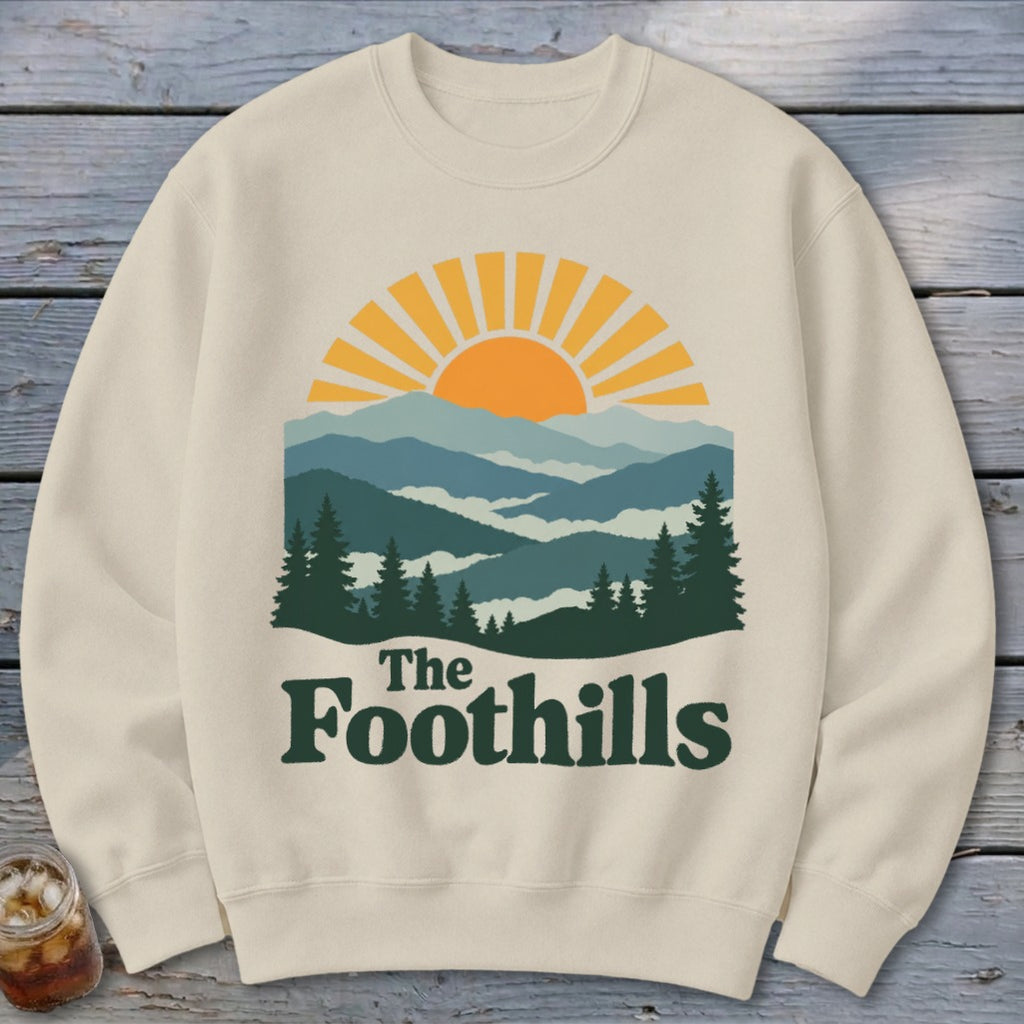Cream sweatshirt with "The Foothills" text and mountain sunset graphic.