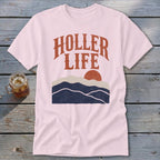 Light pink short-sleeve t-shirt with orange text reading "HOLLER LIFE" over a retro mountain landscape graphic.