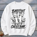 White sweatshirt with a black graphic of bare feet on a rock in water, text reads "Barefoot on the Creek Bank."