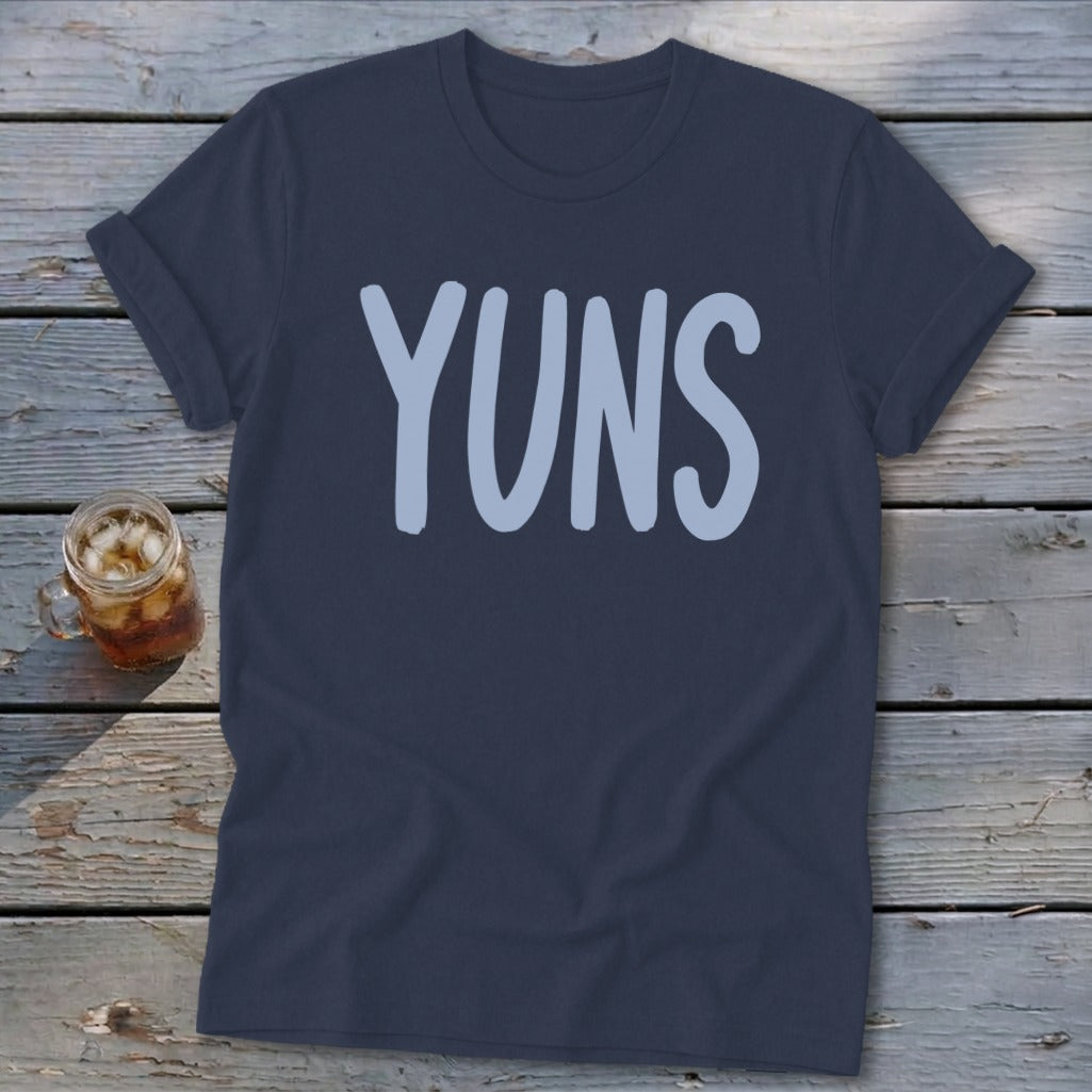 Navy t-shirt with "YUNS" in light blue text, next to a glass of iced tea.