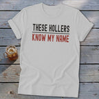 White t-shirt with black text that reads "THESE HOLLERS" above red text that reads "KNOW MY NAME".