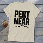 Light cream t-shirt featuring bold black text reading Pert Near above a mountain range graphic.