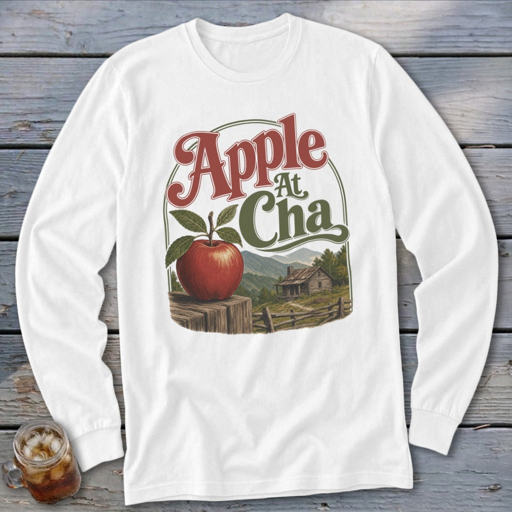 White long-sleeve t-shirt with a vintage graphic of a red apple on a wooden post before a mountain cabin.