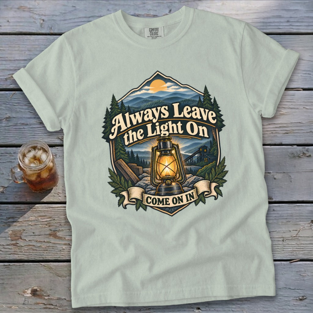 Light green t-shirt with a graphic of a lantern and mountains reading "Always Leave the Light On Come On In."
