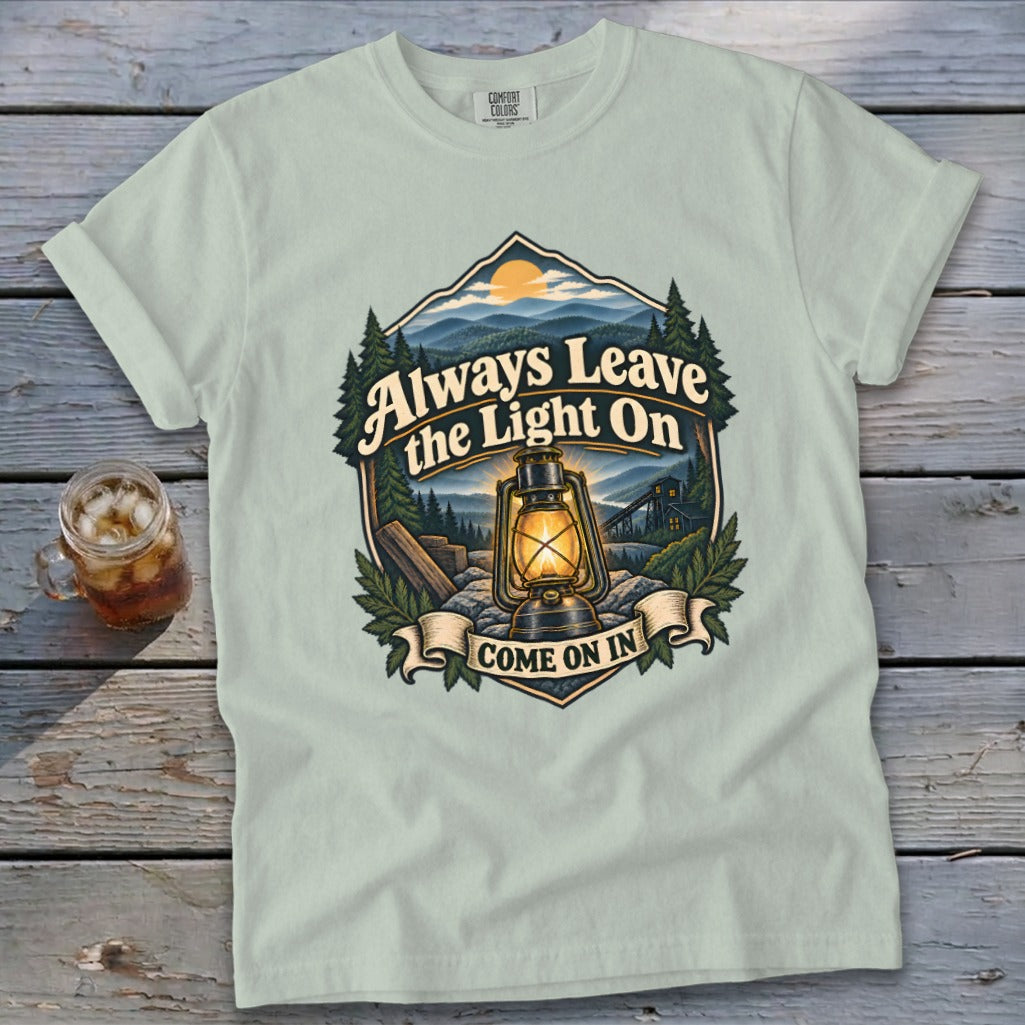 Light green t-shirt with a graphic of a lantern and mountains reading "Always Leave the Light On Come On In."