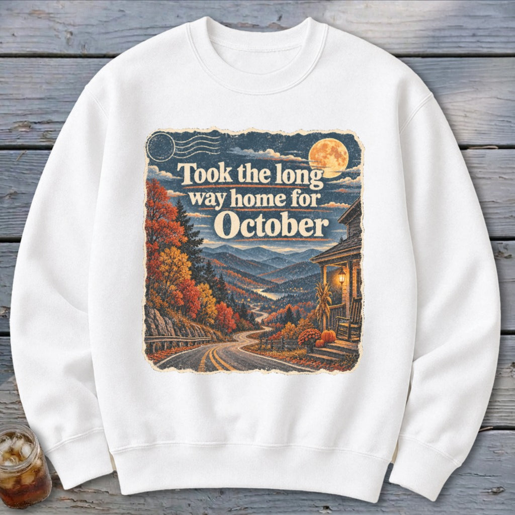 White sweatshirt with a graphic of autumn mountains, road, and house, featuring text "Took the long way home for October".