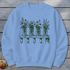 Light blue crewneck sweatshirt featuring a dark green graphic of four mason jars filled with wildflowers sitting on a wooden shelf.