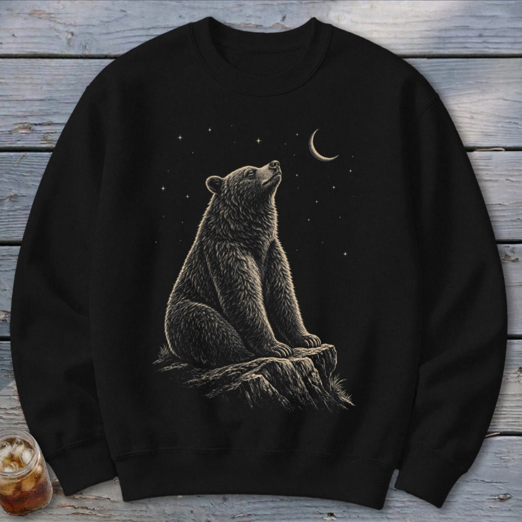 Black crewneck sweatshirt with a bear sitting on a rock under a crescent moon and stars.