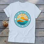 White t-shirt featuring a circular graphic with mountains, a rising sun, and text reading BORN IN THE HOLLER RAISED ON THE RIDGE.