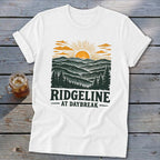 White t-shirt with "RIDGELINE AT DAYBREAK" and mountain sunset graphic.