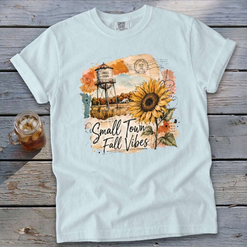 White t-shirt with watercolor graphic of a water tower, sunflower, and text "Small Town Fall Vibes."
