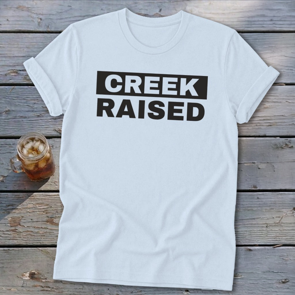 White t-shirt with "CREEK RAISED" in black text on a black background.