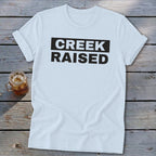 White t-shirt with "CREEK RAISED" in black text on a black background.