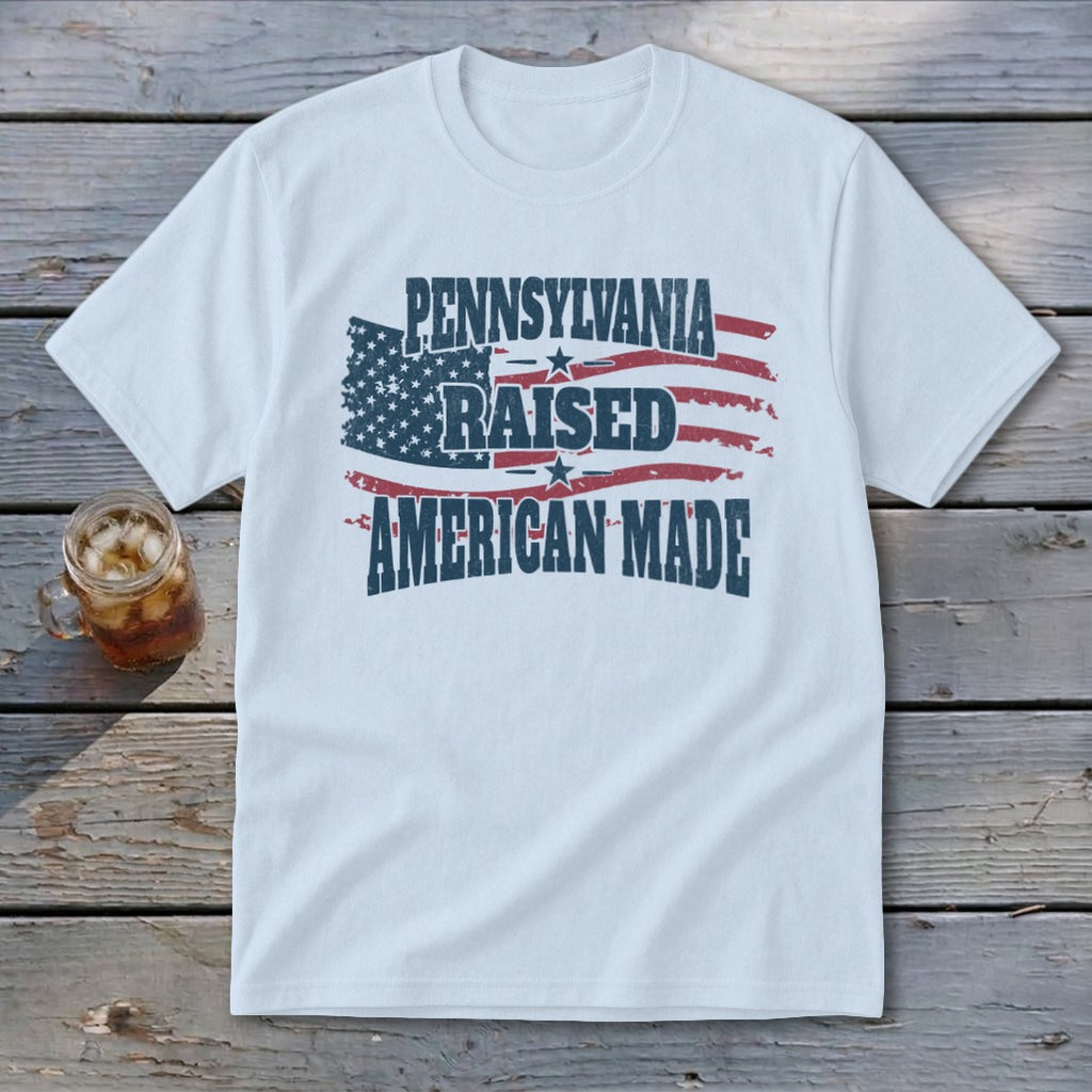 A white crewneck t-shirt featuring the text Pennsylvania Raised American Made overlaid on a distressed American flag graphic.