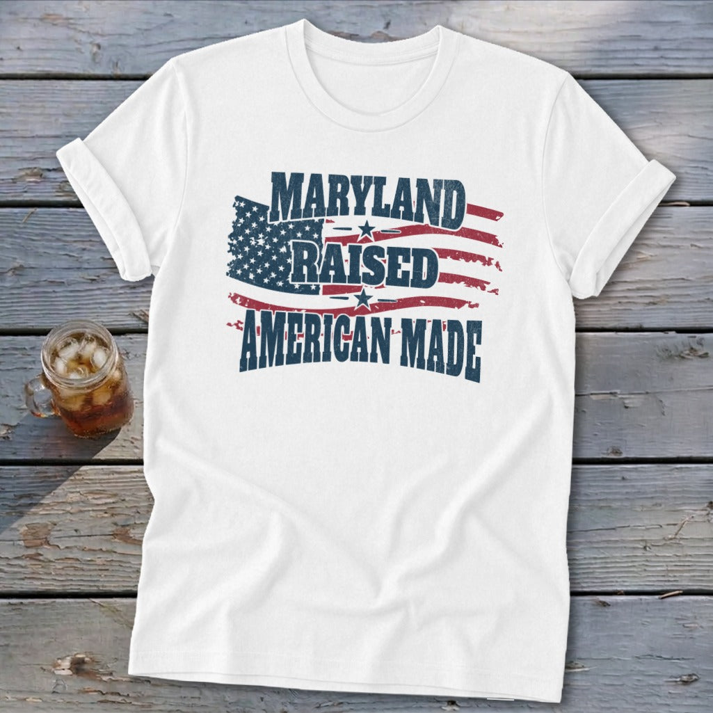 A white t-shirt with a distressed graphic featuring the American flag and the text Maryland Raised American Made.