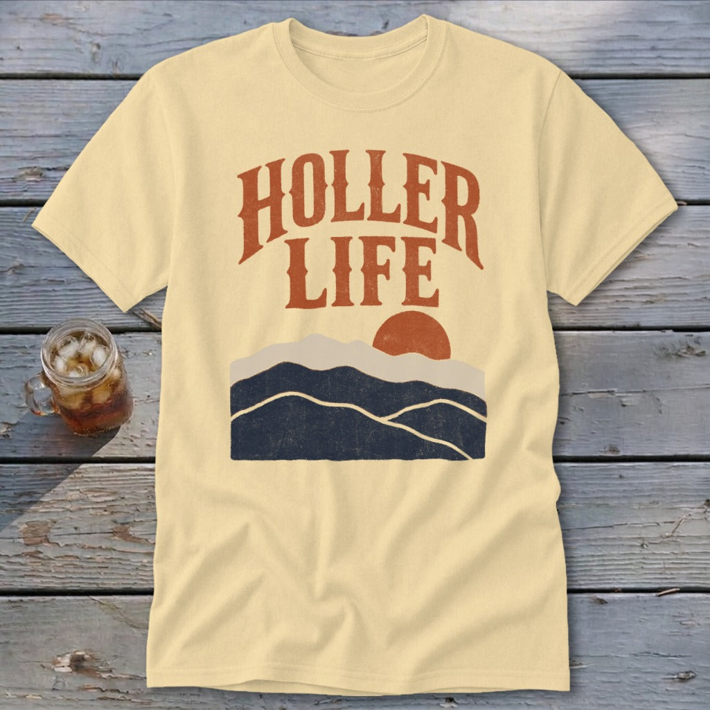 A cream-colored t-shirt with brown text reading "HOLLER LIFE" above a mountain and sun graphic.