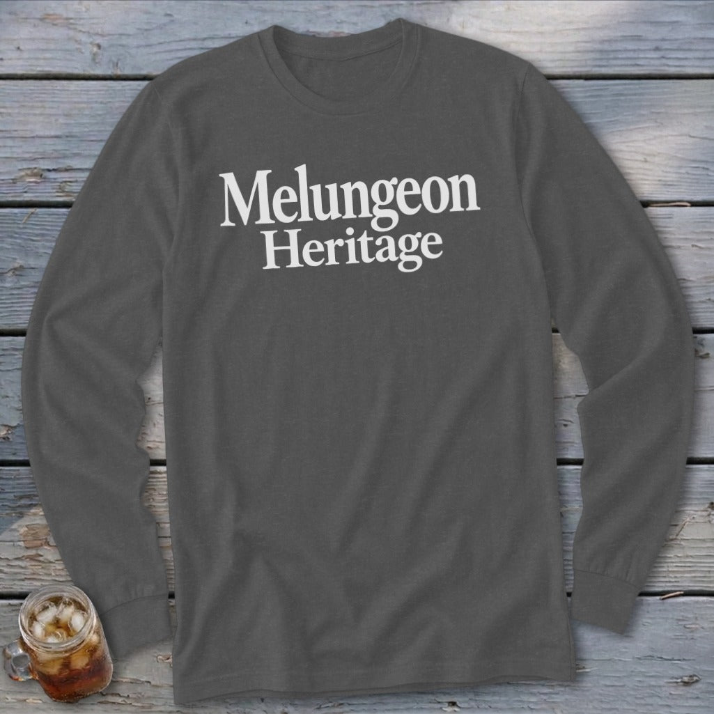 Dark gray long-sleeve t-shirt with white text reading "Melungeon Heritage" centered on the chest, laid flat on a weathered wooden surface.