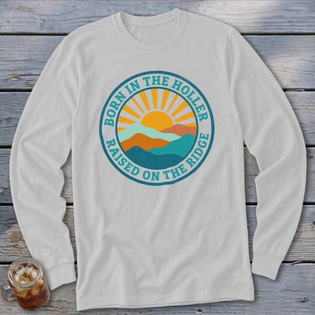 Light gray long-sleeve t-shirt featuring a circular graphic with mountains, a rising sun, and the text Born in the Holler Raised on the Ridge.