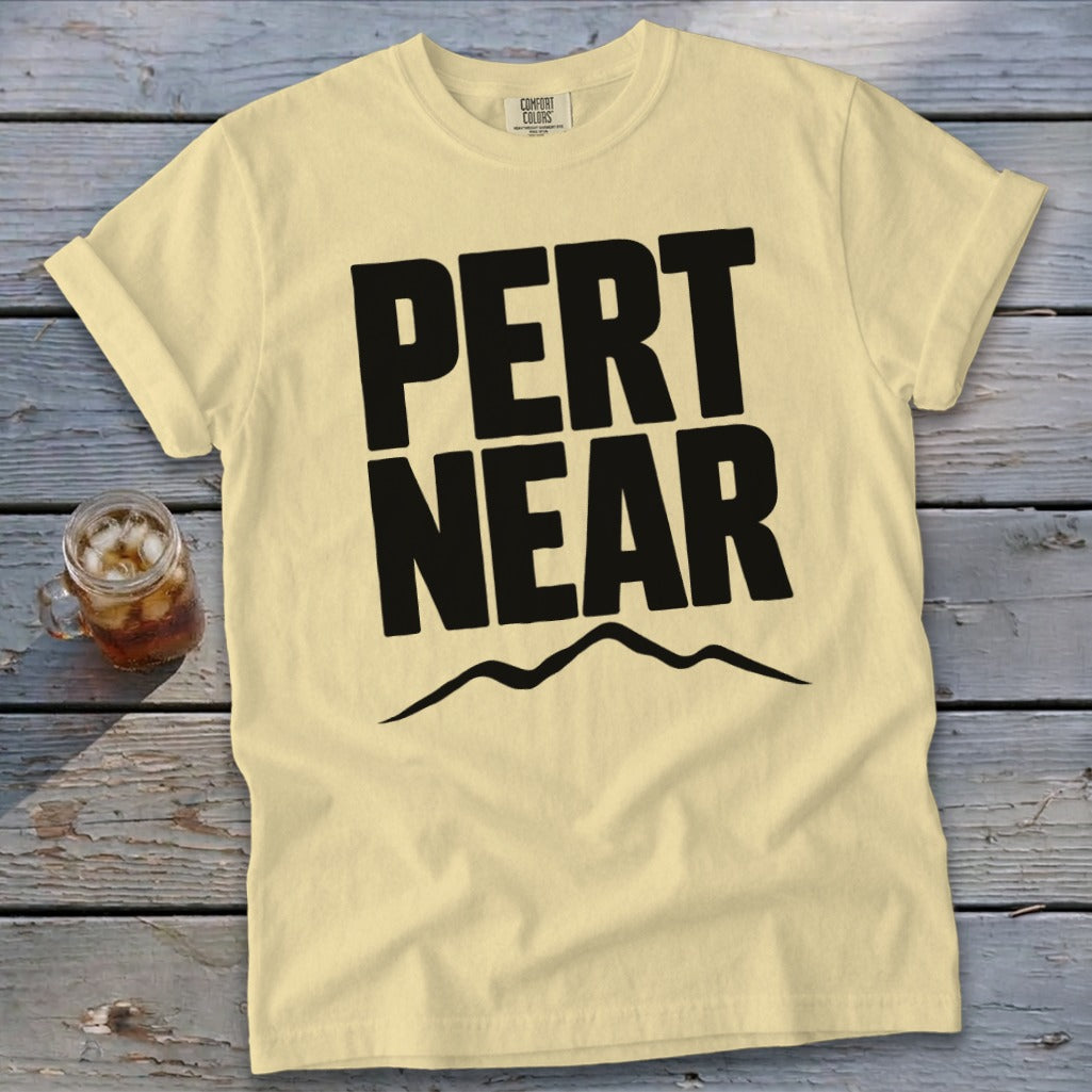 Light yellow short-sleeved t-shirt with bold black text reading PERT NEAR above a mountain outline.