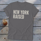 Gray t-shirt with "NEW YORK RAISED" text in white, next to a glass of iced drink.