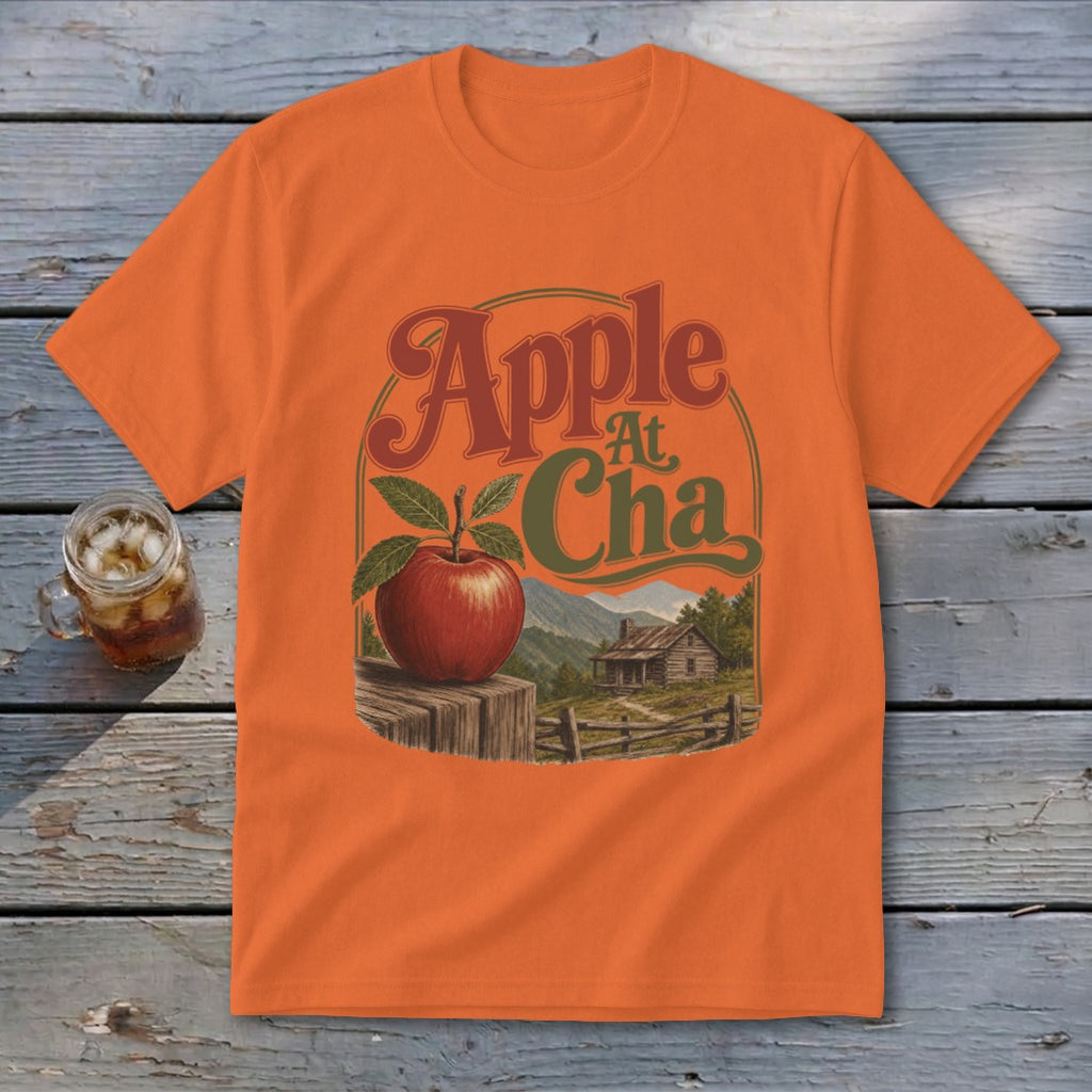 An orange t-shirt featuring a retro graphic of an apple, mountain cabin, and the text Apple At Cha.