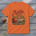 An orange t-shirt featuring a retro graphic of an apple, mountain cabin, and the text Apple At Cha.