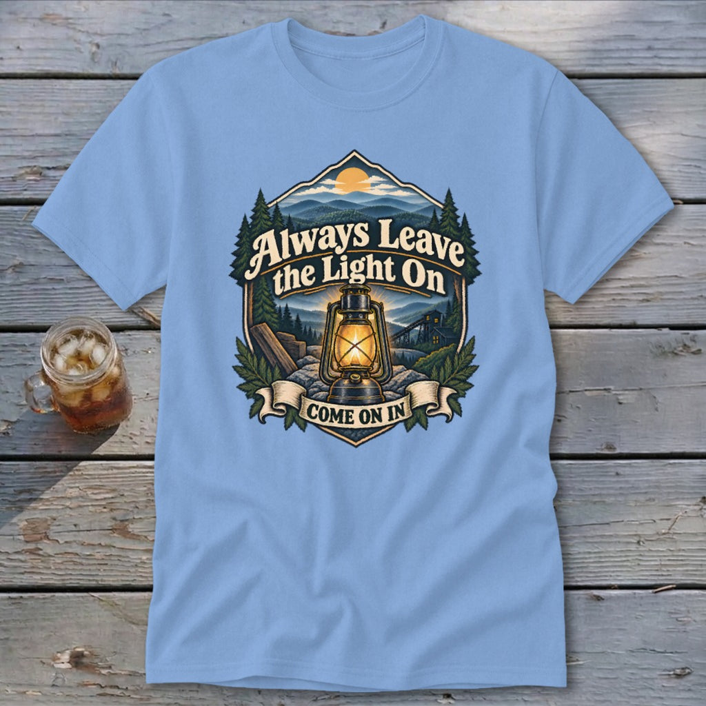 Light blue t-shirt with a graphic of a lantern, mountains, and text "Always Leave the Light On Come On In".