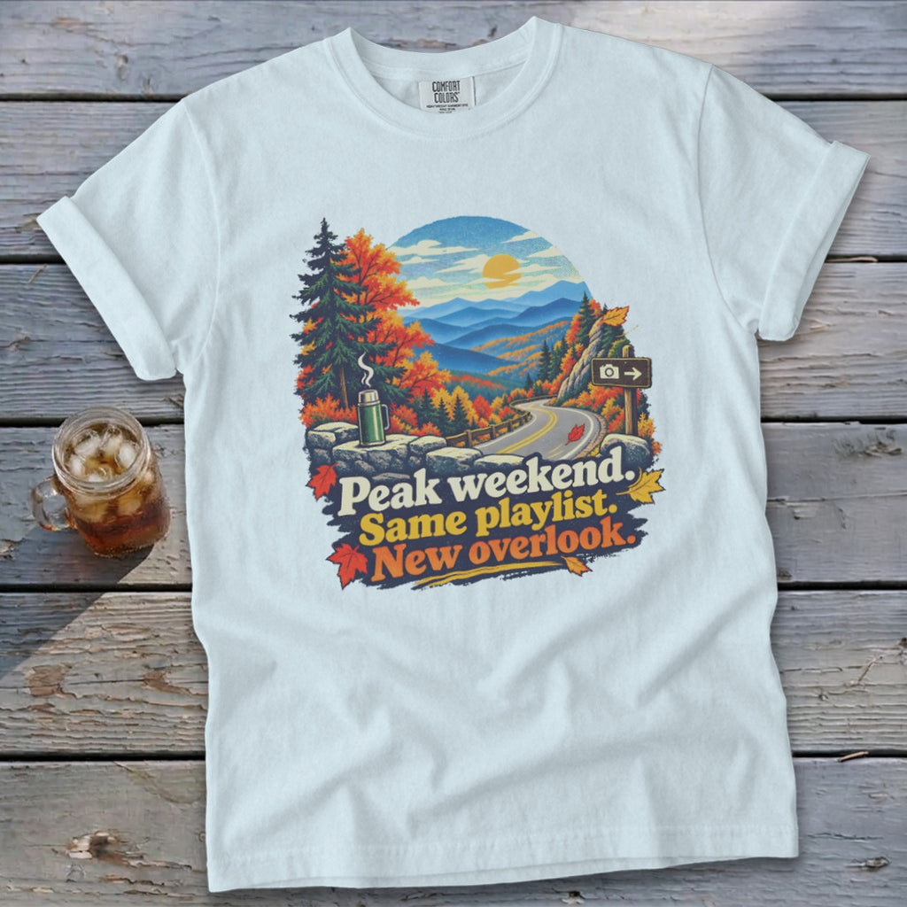 White t-shirt with autumn mountain overlook graphic and text "Peak weekend. Same playlist. New overlook."