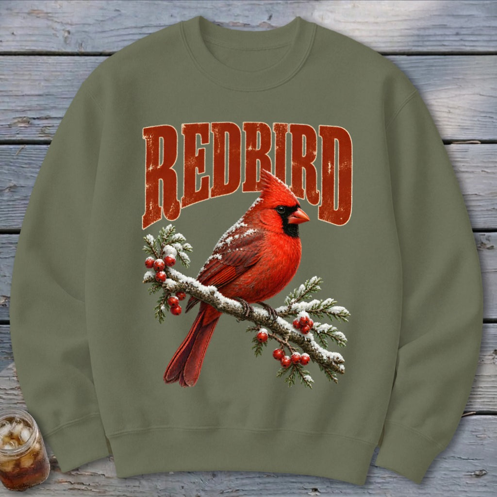 An olive green crewneck sweatshirt with a graphic of a red cardinal on a snow-covered branch and the text REDBIRD.