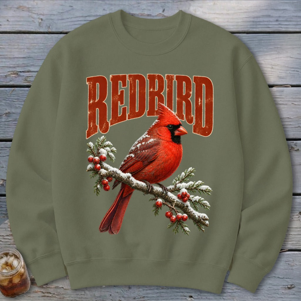 An olive green crewneck sweatshirt with a graphic of a red cardinal on a snow-covered branch and the text REDBIRD.