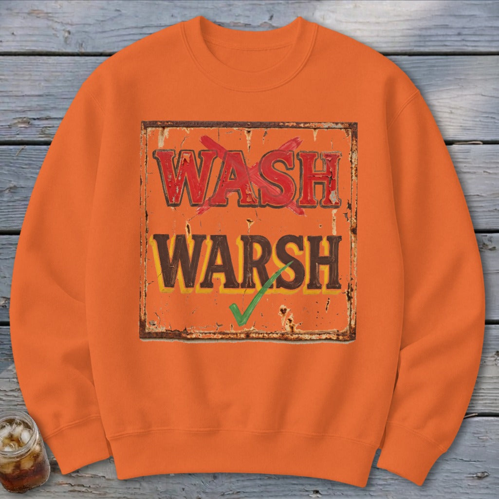 An orange crewneck sweatshirt printed with a weathered sign showing Wash crossed out and Warsh checked.