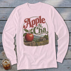 A light pink long-sleeve shirt featuring a retro graphic of an apple, a cabin, and mountains.