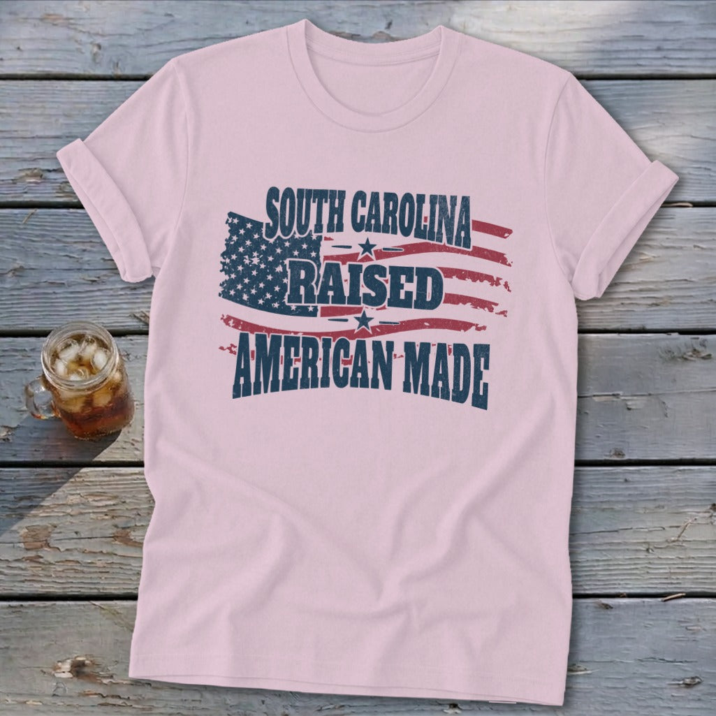 Pink t-shirt with "South Carolina Raised American Made" text over distressed American flag graphic.